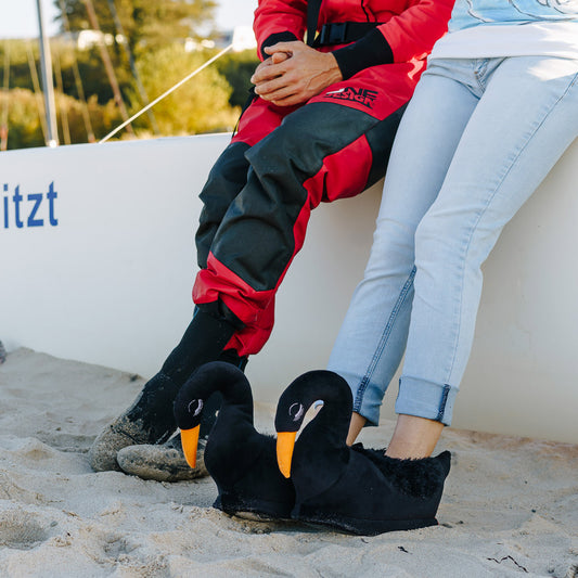 Person am Strand trägt schwarze Schwan Hausschuhe